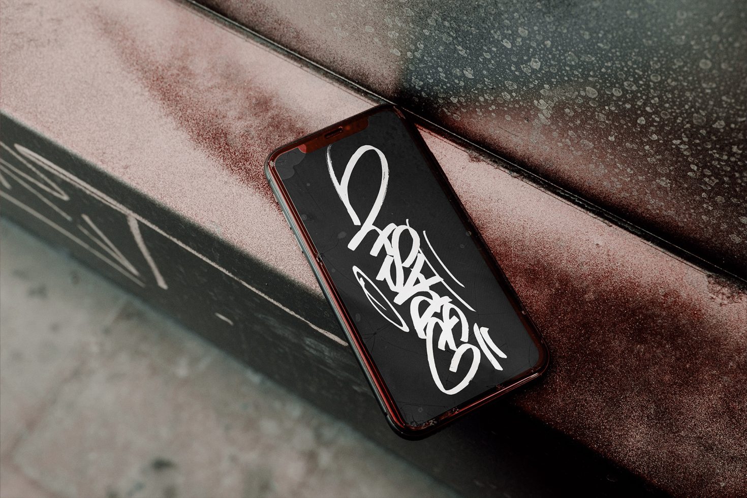 Smartphone with graffiti-style font design on screen resting on a dusty metallic surface, showcasing urban font mockup for graphic design.